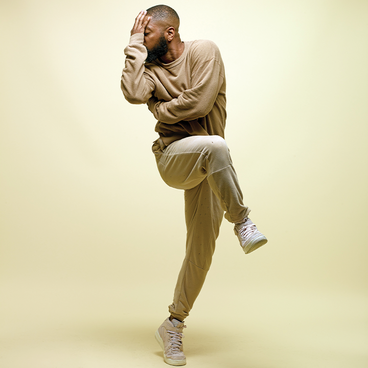 A man standing on one leg while hiding his face